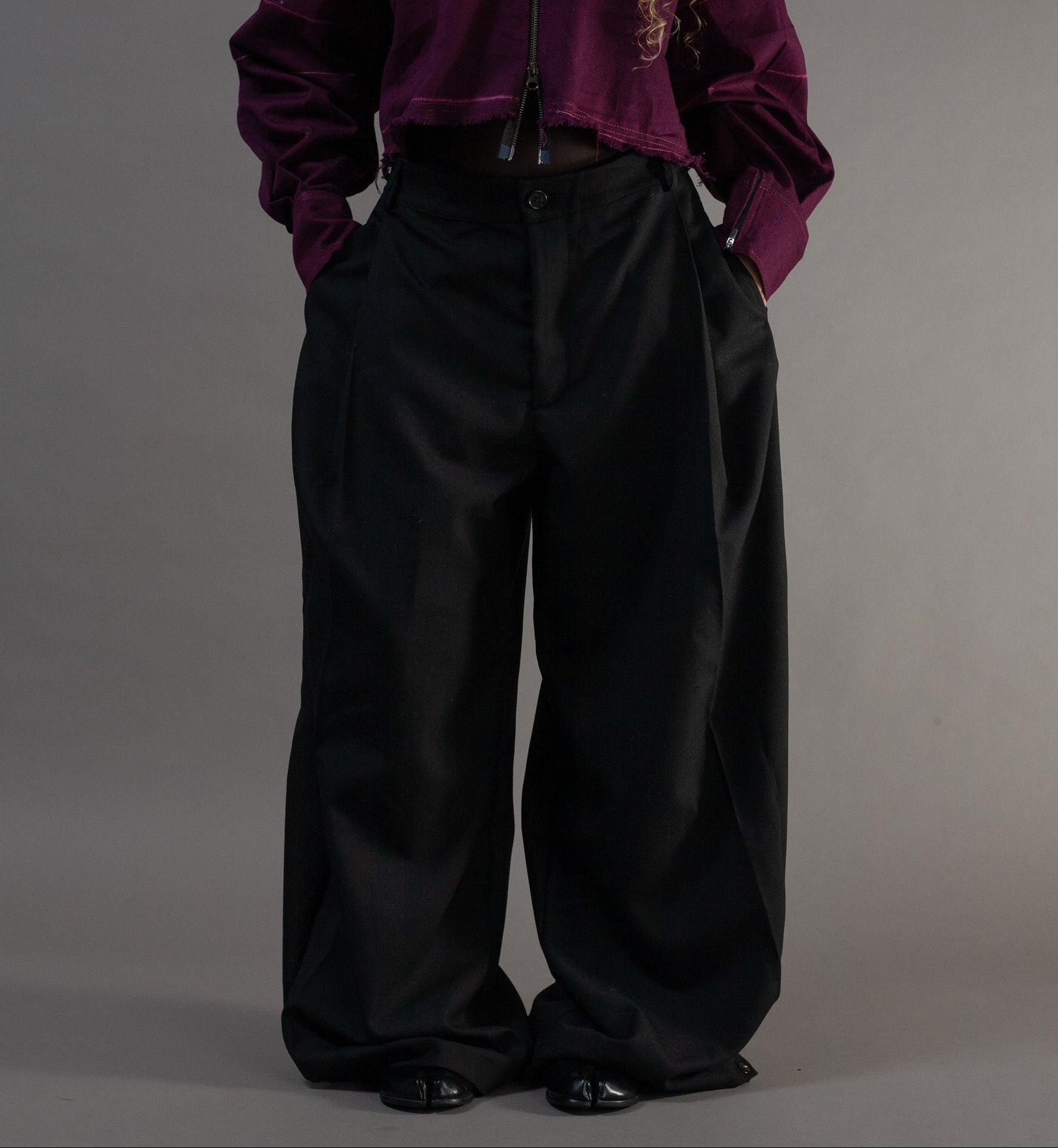 Person wearing a purple jacket and black pants on a grey background