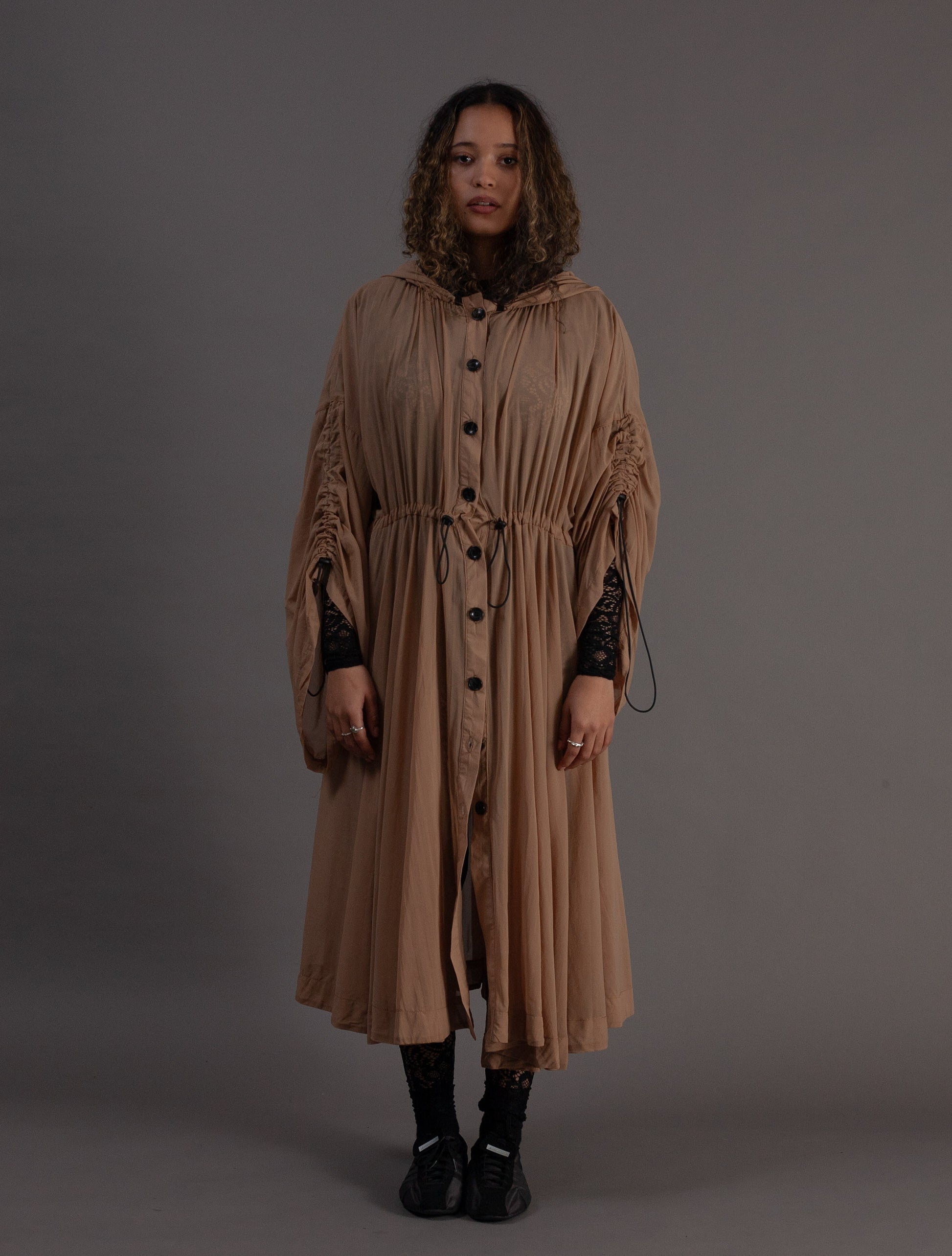 Woman wearing a long beige dress with black buttons against a grey background