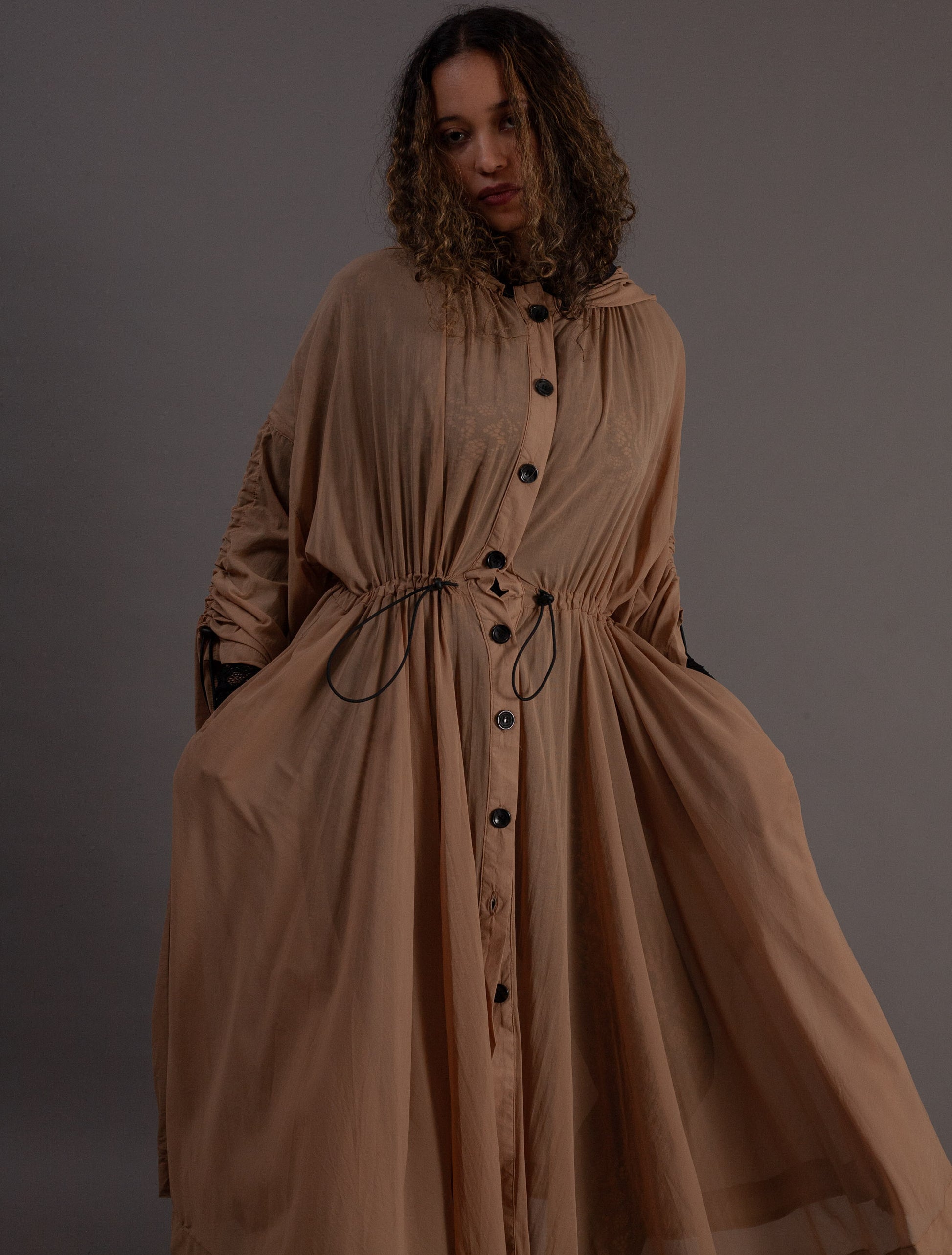 Woman wearing a long beige dress with black buttons 