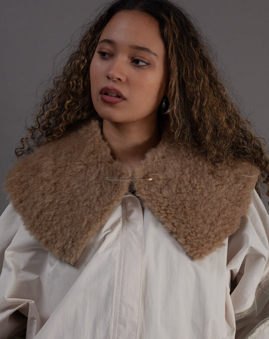 Woman wearing a beige coat with a fur collar against a grey background
