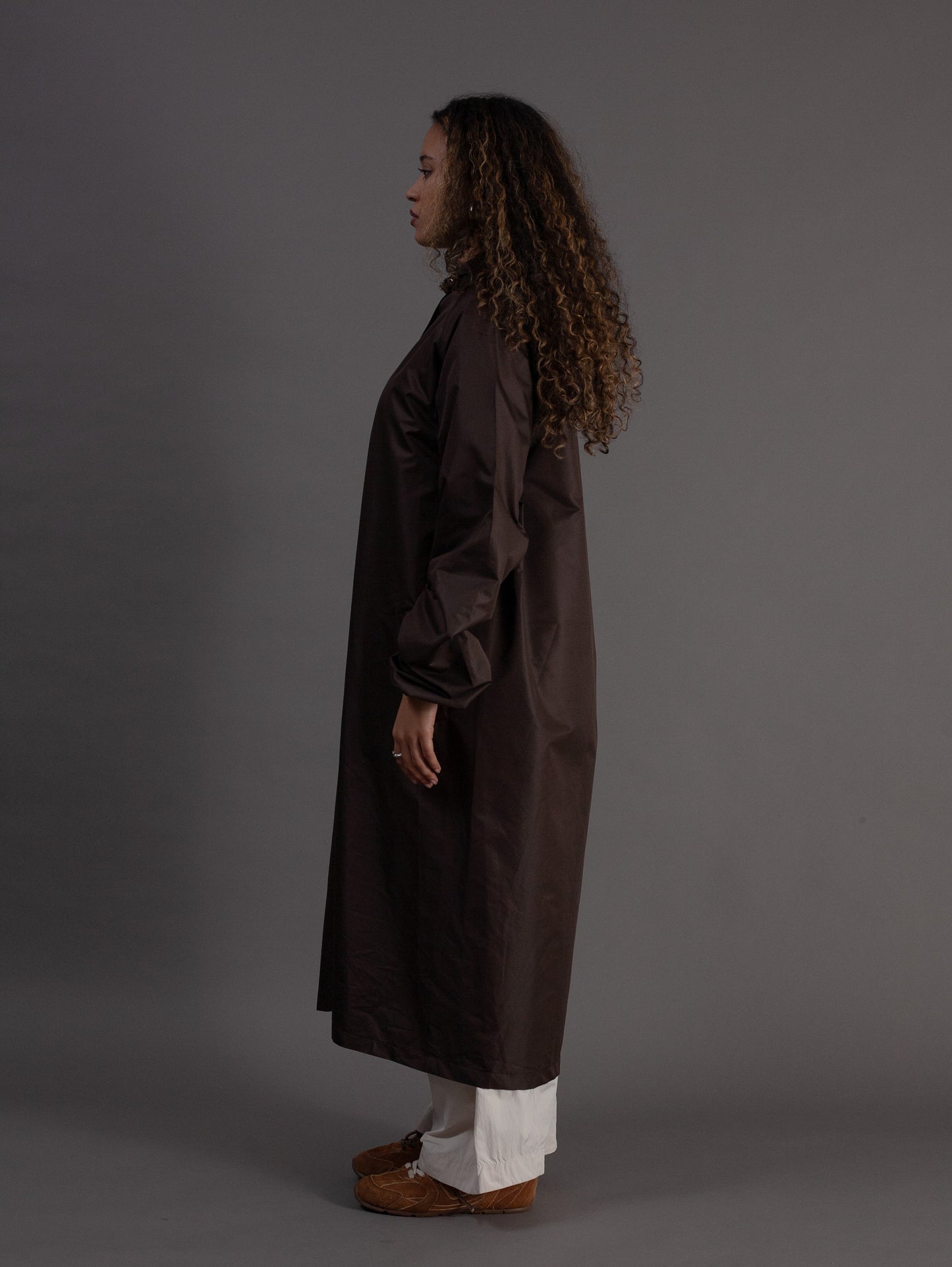 Person wearing a long brown coat against a grey background