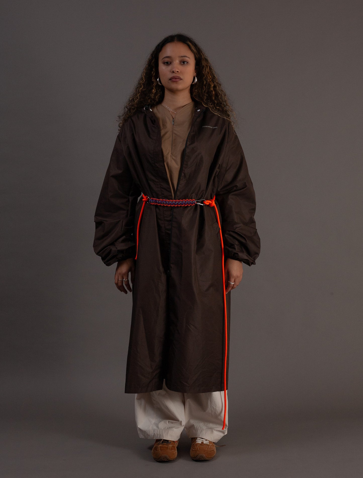 Person wearing a long dark chocolate raincoat with orange accents on a grey background