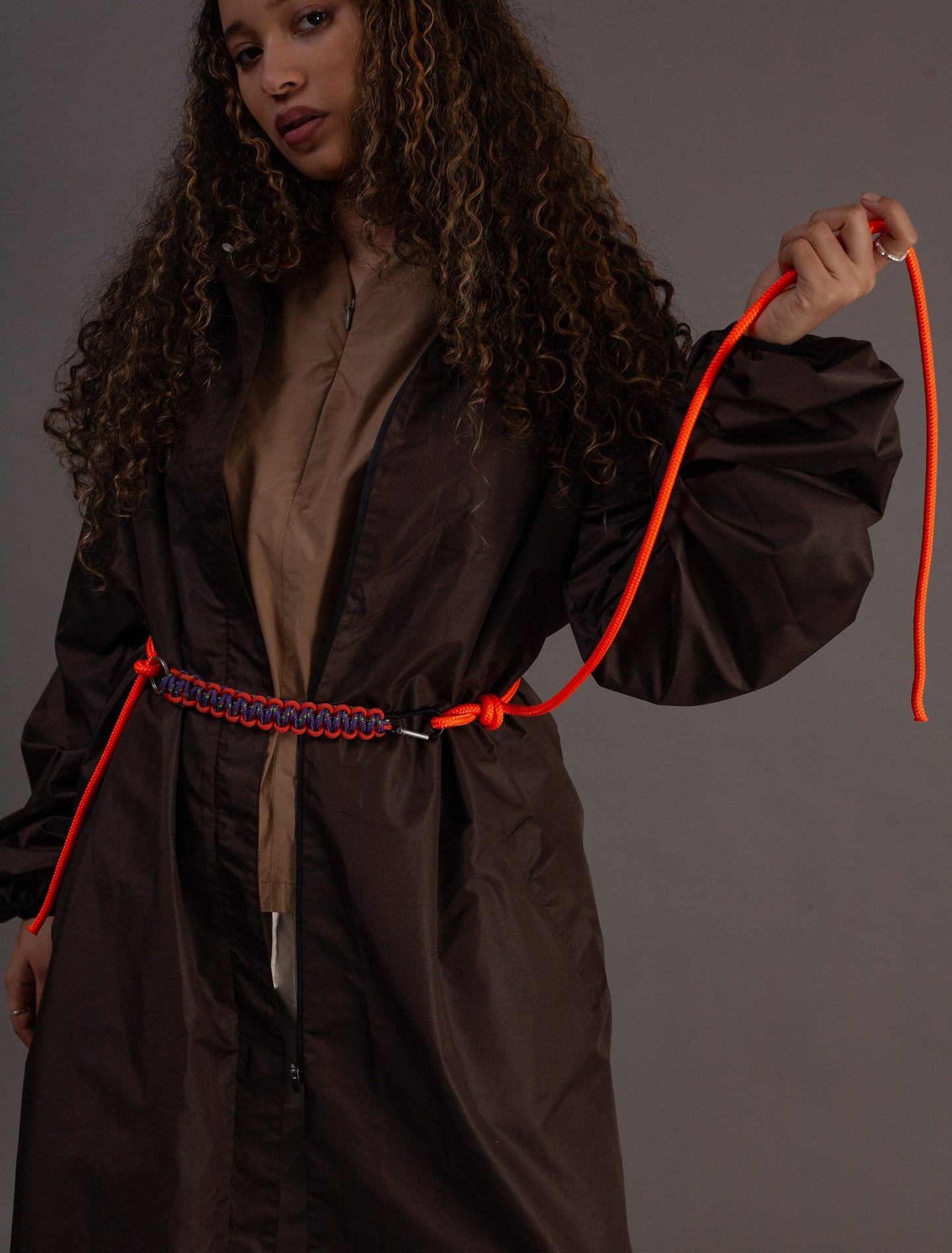 Person wearing a dbrown coat holding an orange rope against a grey background