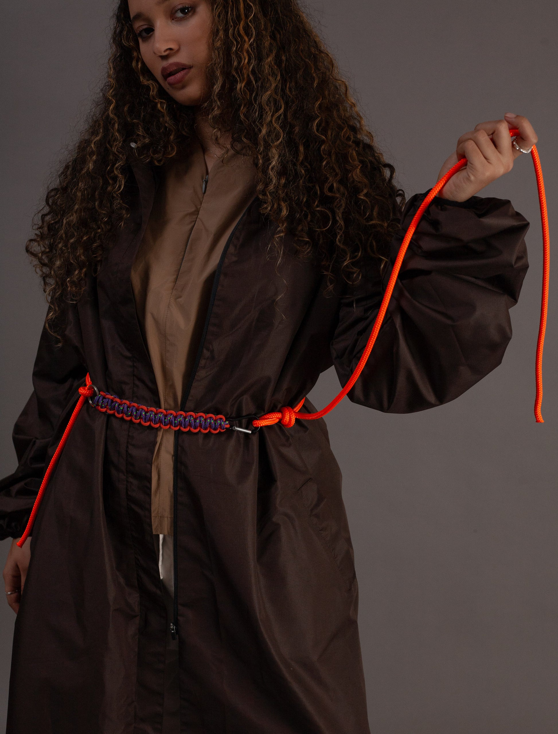 Person wearing a dbrown coat holding an orange rope against a grey background